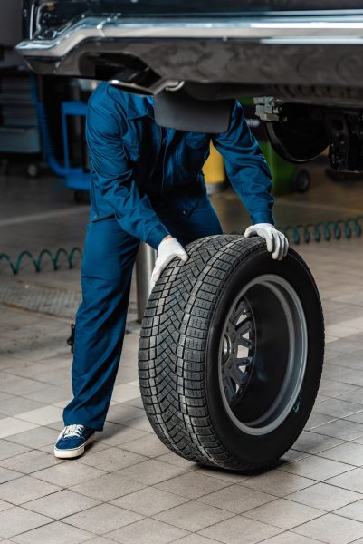 cropped view of mechanic with wheel near raised car in workshop